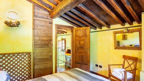 Une pièce avec un lit, des poutres en bois au plafond, une porte en bois, une chaise avec une serviette et un miroir au mur.