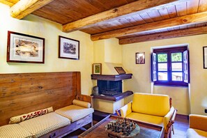 Una habitación acogedora con vigas de madera, chimenea, sofá, sillón amarillo y cuadros enmarcados en la pared.