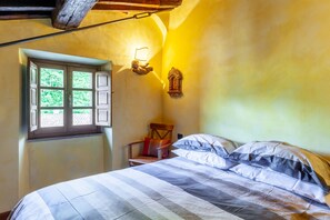 Un dormitorio con cama, una silla, un ventanal y una lámpara fijada a la pared.