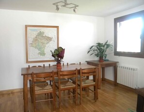 A dining area with a wooden table and chairs, a map on the wall, a potted plant, and a window with natural light. - Apartment 'Ultzama' with Mountain View and Balcony (Iraitzoz)