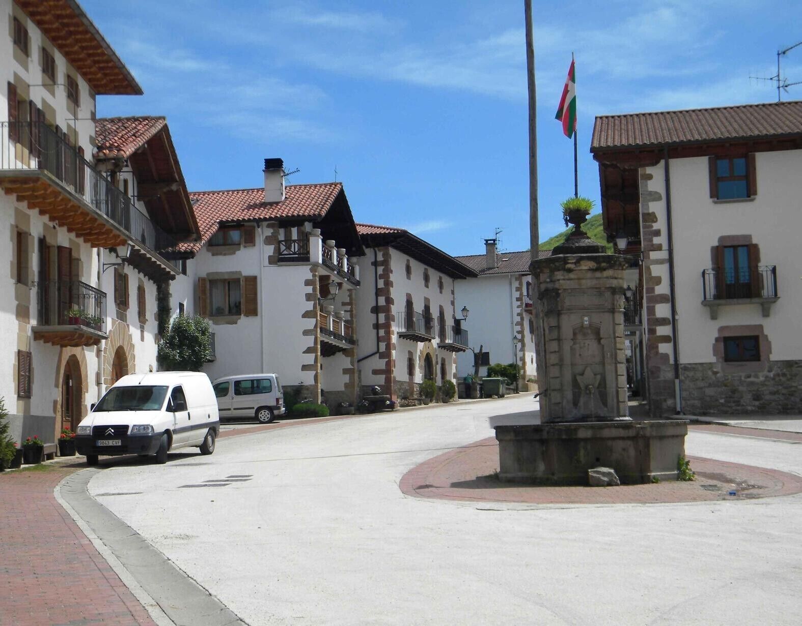 Una calle con edificios, una bandera y una fuente.