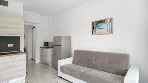 Eine moderne Küche mit weißen Schränken, einem grauen Sofa und einem Gemälde mit Strandmotiv.