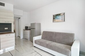 Une cuisine moderne avec des meubles blancs, un canapé gris et un tableau représentant une scène de plage.