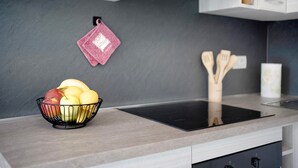 Eine Küche mit einer schwarzen Induktionskochplatte, einer Obstschale auf der Arbeitsfläche und hängenden Holzkochinstrumenten an der Wand.