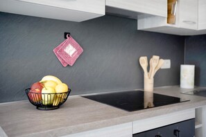 Une cuisine dotée d’une plaque de cuisson à induction noire, d’un saladier de fruits posé sur le plan de travail et d’ustensiles en bois accrochés au mur.