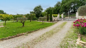 A gravel path leading to a gated entrance, surrounded by greenery and trees.