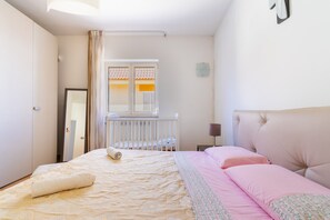 Een slaapkamer met een bed, een raam met gordijnen, een nachtkastje en een wandlamp.