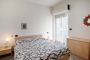 A bedroom with a bed, bedside tables, a dresser, a wall-mounted mirror, and a window with curtains.