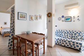 A room with a wooden dining table, chairs, a sofa with a blue and white pattern, and a bed with a blue and white bedspread.