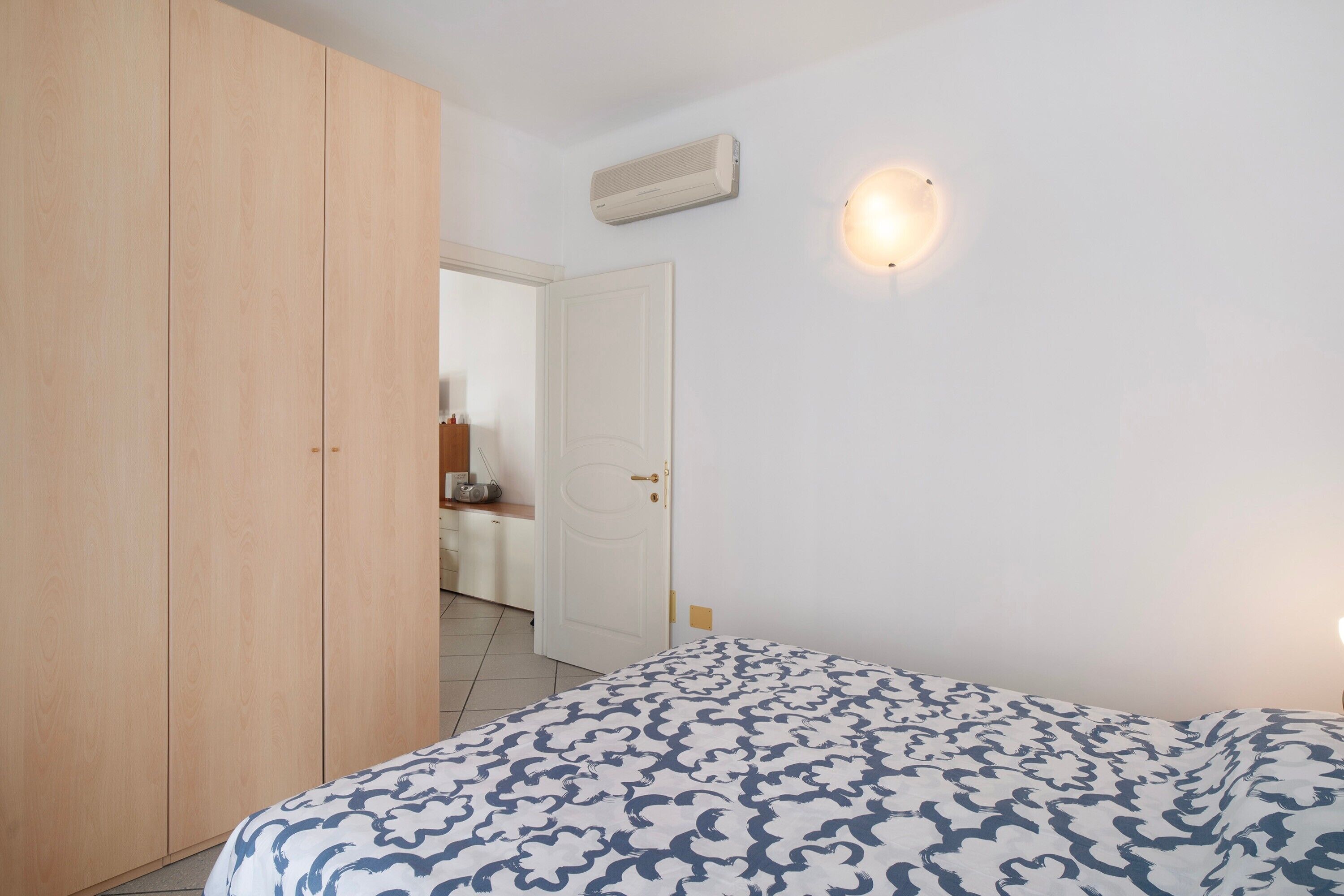 A bedroom with a bed, wardrobe, and a wall-mounted air conditioner.