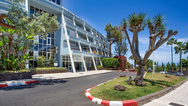 A modern hotel with a multi-story structure, a landscaped entrance, and a clear sky. - Vacation Apartment 'Casa Ana' with Sea and Teide View, Shared Pool and Wi-Fi (SANTA URSULA)