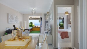 A modern living room with a dining area, a view of the outdoors, and a bedroom with a balcony. - Vacation Apartment 'Casa Ana' with Sea and Teide View, Shared Pool and Wi-Fi (SANTA URSULA)