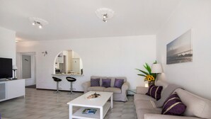 A modern living room with a white coffee table, a beige sofa, and a dining area with a white countertop and bar stools. - Casa Solimmo' with Sea View, Wi-Fi and Air Conditioning (Quarteira)