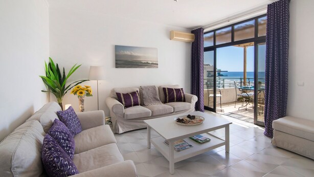 A living room with a sofa, coffee table, and a view of the sea through large windows. - Casa Solimmo' with Sea View, Wi-Fi and Air Conditioning (Quarteira)