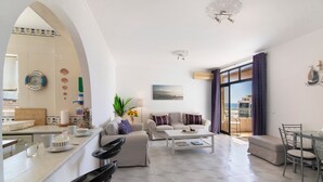 A spacious living area with a sofa, coffee table, and dining table. There is a kitchen area with a counter and a sink. - Casa Solimmo' with Sea View, Wi-Fi and Air Conditioning (Quarteira)