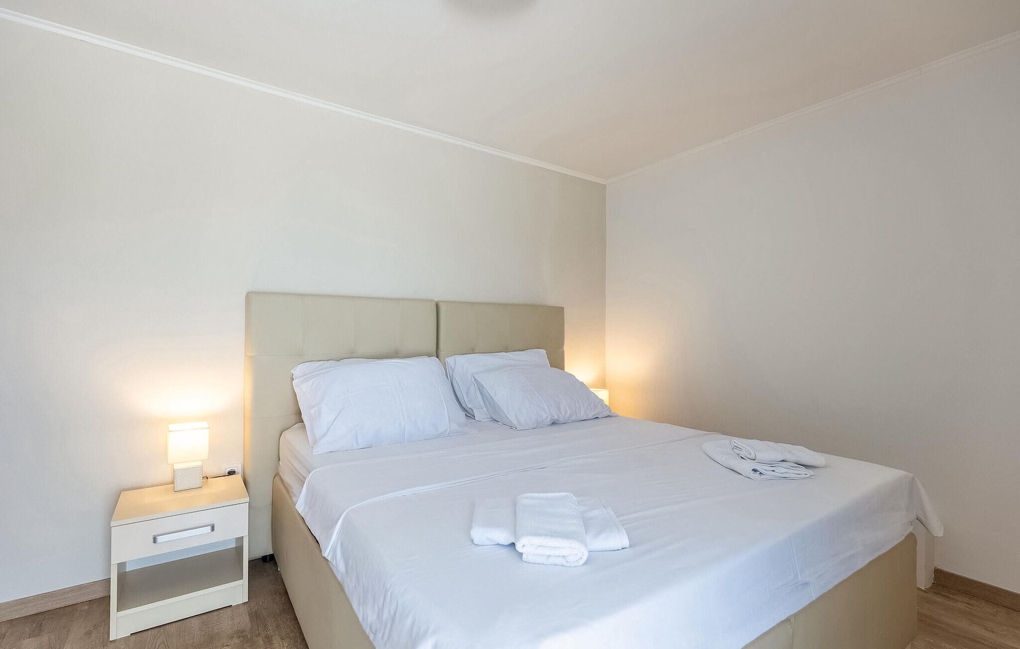 A neatly made bed with white linens and pillows, a bedside table with a lamp, and a folded towel on the bed.