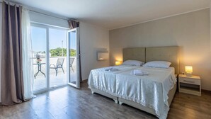 A hotel room with a bed, a nightstand, a lamp, a sliding glass door to a balcony, and a view of the outdoors.