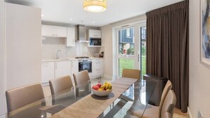 A modern kitchen with white cabinets, a dining area with a glass table, and a view of the outdoors. - Modern 3BR Flat quick links to LDN and Heathrow (Surrey)