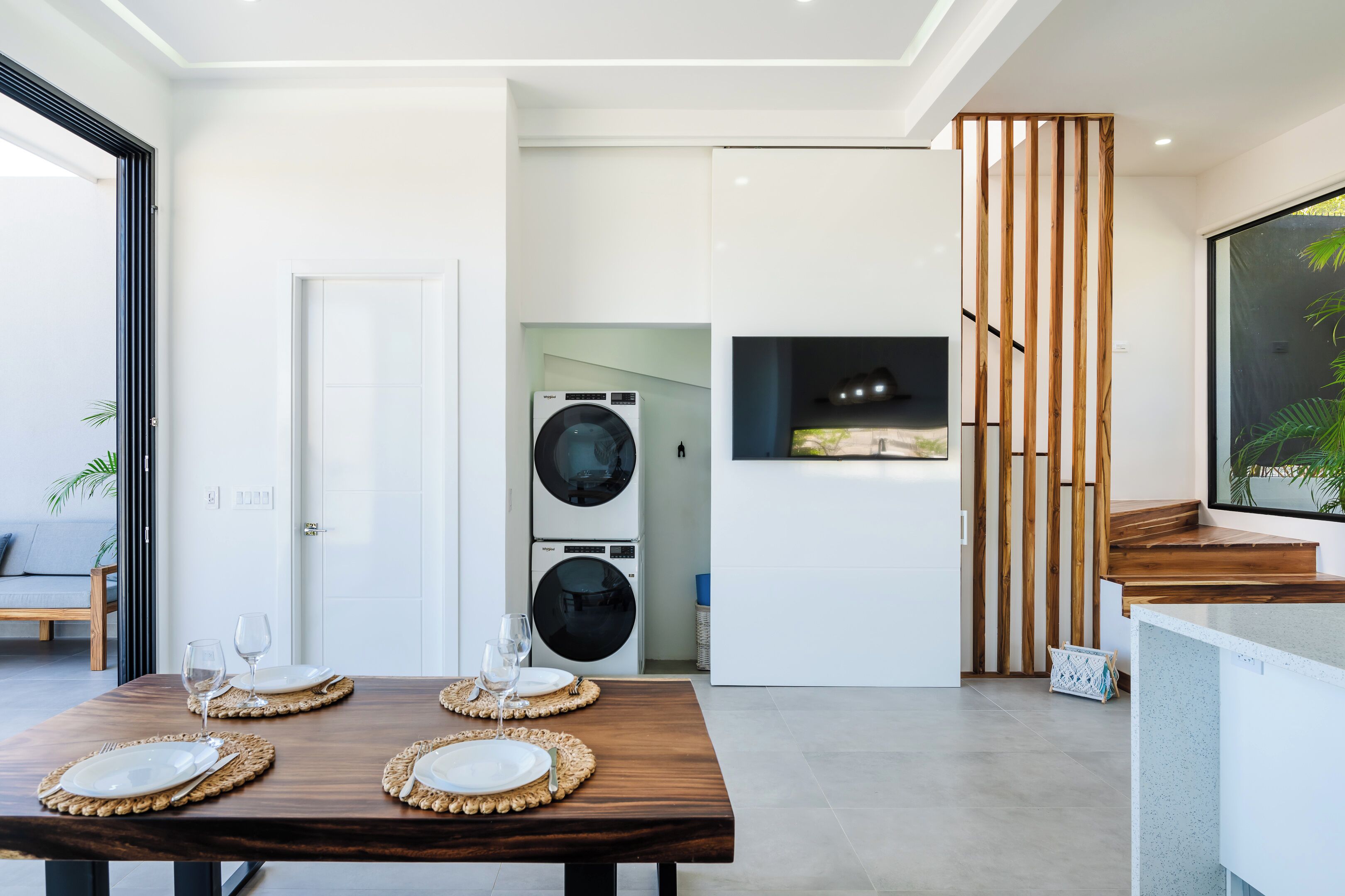 A modern kitchen with built-in appliances, a dining area with a wooden table set for four, and a large window overlooking the outdoors.