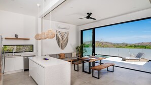 Una cocina moderna con armarios blancos, una isla central y una zona de comedor con mesa y bancos.