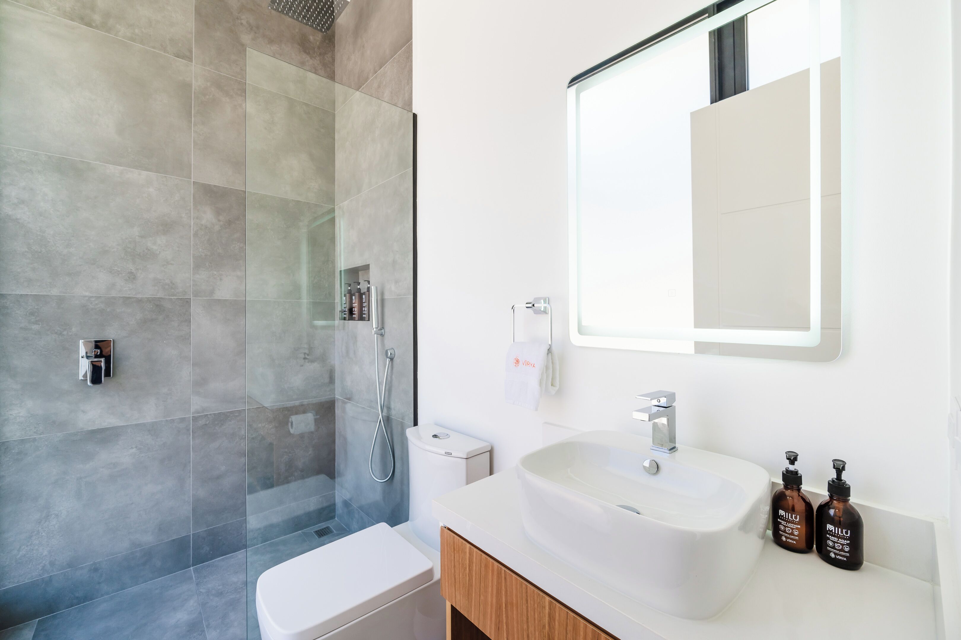 Un bagno moderno con cabina doccia in vetro, un water bianco e un lavandino con due flaconi di shampoo.