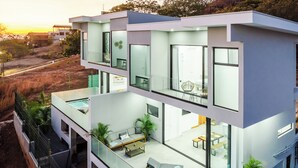 Una casa moderna de varios pisos con balcón de vidrio, mobiliario exterior y piscina.