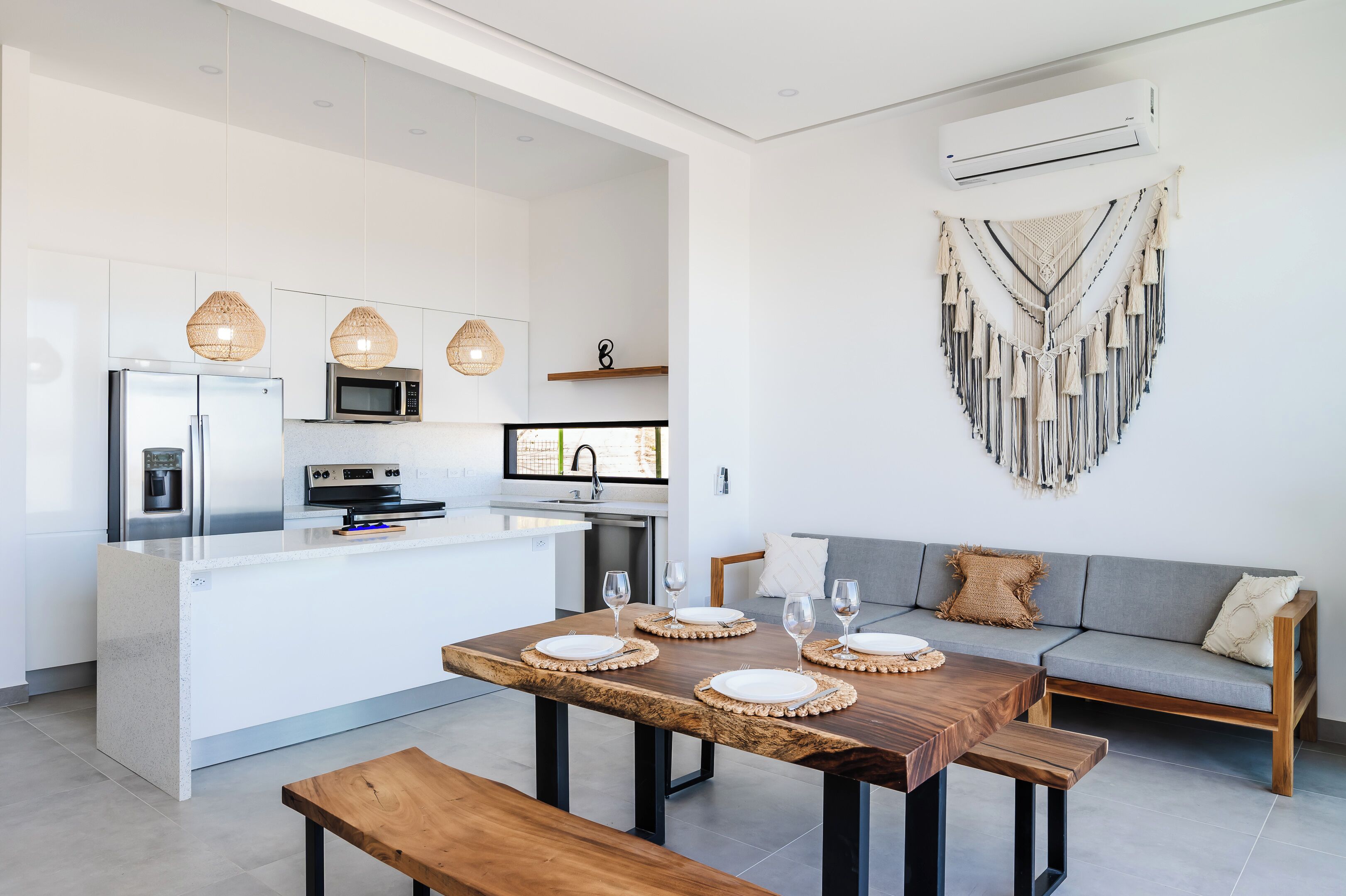 A modern kitchen with white cabinetry, a central island, and a dining area with a wooden table and benches.