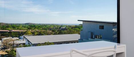 Un balcón con una mesa y una silla blancos, con vista a una zona residencial con casas y vegetación.