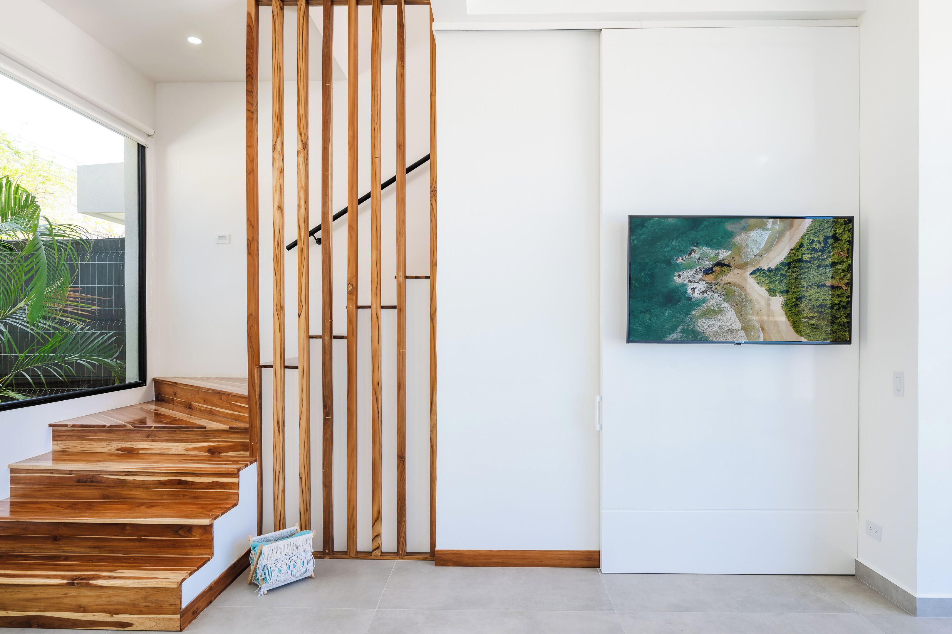 A staircase with wooden steps and a wooden panel divider, a framed picture of a coastal landscape on the wall, and a plant near the window.