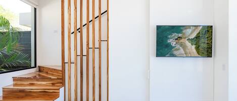 A staircase with wooden steps and a wooden panel divider, a framed picture of a coastal landscape on the wall, and a plant near the window.