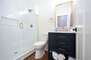 Bathroom features a glass-enclosed shower, toilet, and vanity with gold handles.