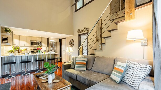 A modern kitchen with a bar area, a grey sofa with patterned cushions, and a staircase with a 'Park City' sign. - Remodeled with Community Amenities in the Canyons Village (Park City)