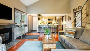 A modern living room with a fireplace, a sofa, a coffee table, and a kitchen in the background. - Remodeled with Community Amenities in the Canyons Village (Park City)