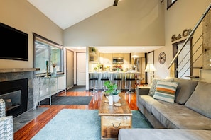 A modern living room with a fireplace, a sofa, a coffee table, and a kitchen in the background. - Remodeled with Community Amenities in the Canyons Village (Park City)