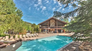 A pool area with lounge chairs and a building with a stone facade. - Remodeled with Community Amenities in the Canyons Village (Park City)