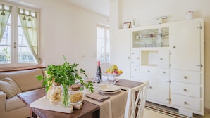 Un coin repas avec une table en bois dressée pour deux personnes, un canapé et un buffet blanc aux portes vitrées.