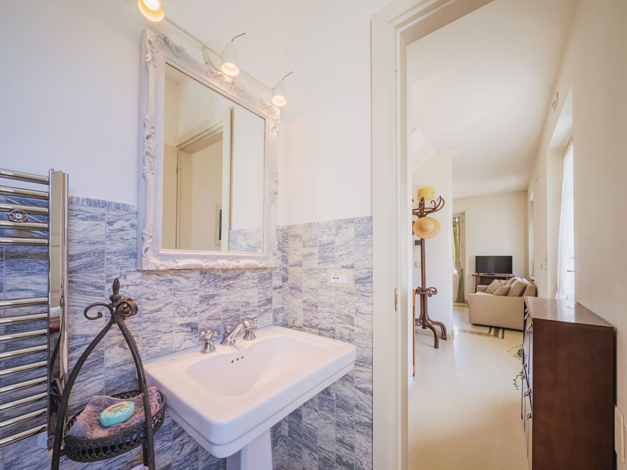 Une salle de bain avec un pare-feu en marbre, un lavabo blanc et un grand miroir.