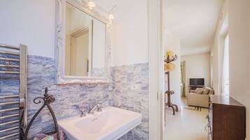 Une salle de bain avec un pare-feu en marbre, un lavabo blanc et un grand miroir.