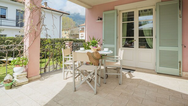Une terrasse couverte avec une table et des chaises, un pot de fleurs et une vue sur les environs.