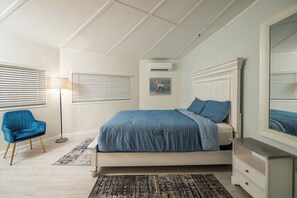 Ein Schlafzimmer mit einem Bett, einem Sessel, einem Nachttisch und einem großen Spiegel.