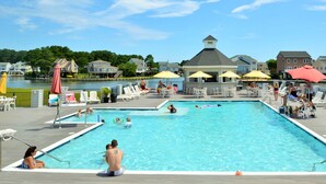 A rectangular swimming pool with a deck area, surrounded by lounge chairs and umbrellas. - Anchor's Away | Captain's Cove Waterfront w/ Pool & Golf, Pet Friendly + First-Floor Suite (Greenbackville)