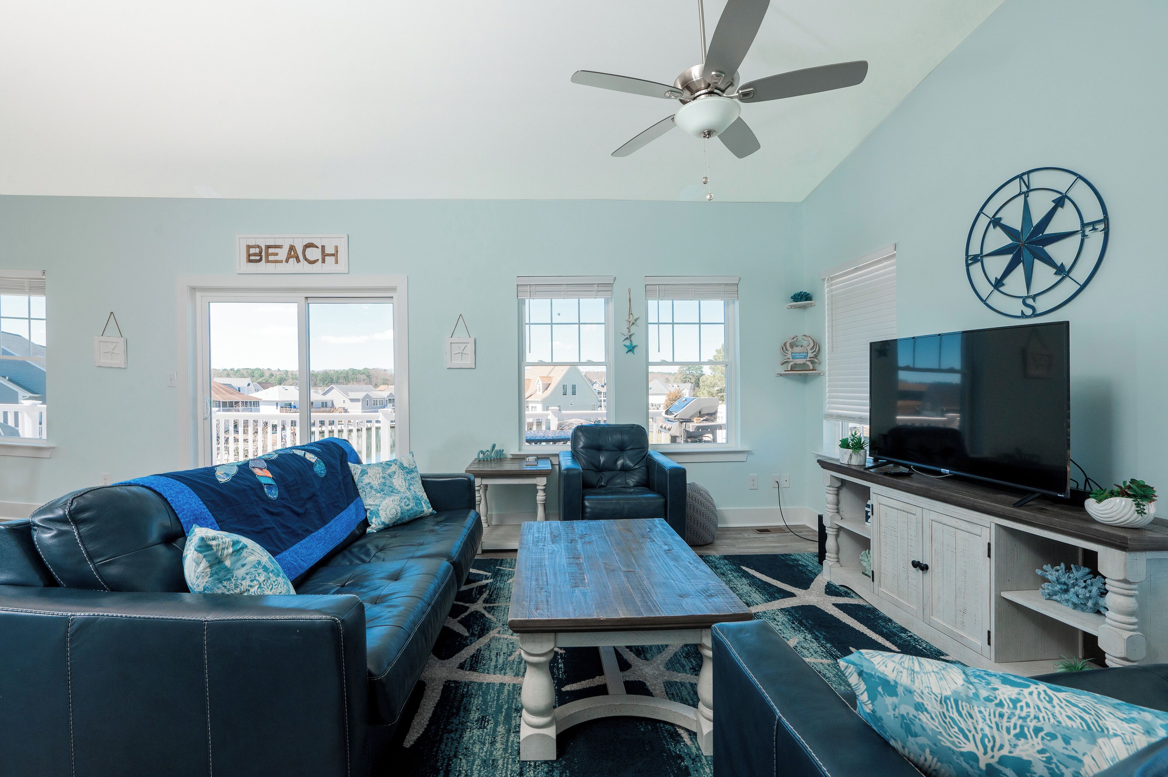 A living room with a sofa, coffee table, and TV, a ceiling fan, and a view of the outside.