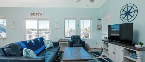 A living room with a sofa, coffee table, and TV, a ceiling fan, and a view of the outside.