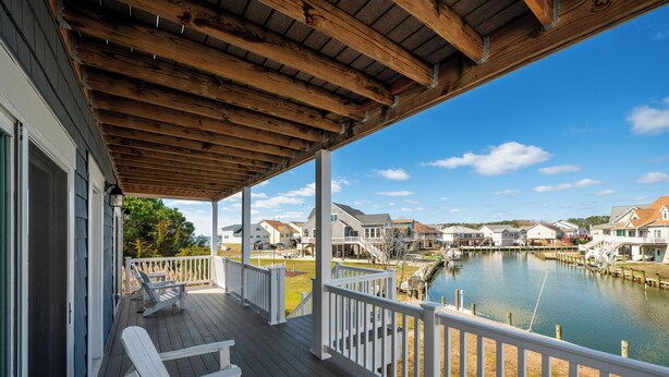A wooden deck with white railings overlooking a calm water body and residential buildings. - Anchor's Away | Captain's Cove Waterfront w/ Pool & Golf, Pet Friendly + First-Floor Suite (Greenbackville)