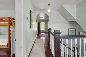 A hallway with a bunk bed, wooden flooring, white walls, and a staircase with white balusters. - Shore Reflections | Restored Victorian Retreat Near Cape Charles, Spacious & Charming (Cape Charles)