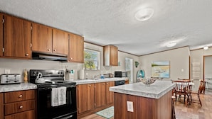 A modern kitchen with wooden cabinets, a central island, and a dining area with wooden chairs.