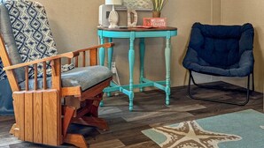 A room with a wooden chair, a blue armchair, a small table with a lamp, a framed picture, and a starfish rug.