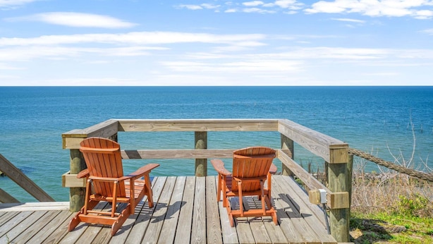 En træterrasse med to træstole, der vender ud mod havet.