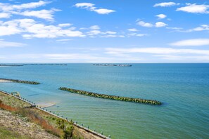 A coastal view with a clear sky, calm water, and a wooden walkway along the shore. - Sunset on the Rocks | 4BR Bayview Butler's Bluff Retreat w/ Game Room + Pet Friendly (Cape Charles)