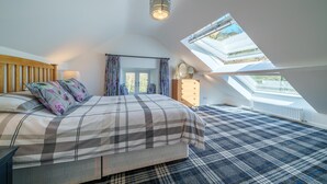 Une chambre avec un puits de lumière, un lit recouvert d’une couverture à carreaux, une commode et une fenêtre avec des rideaux.